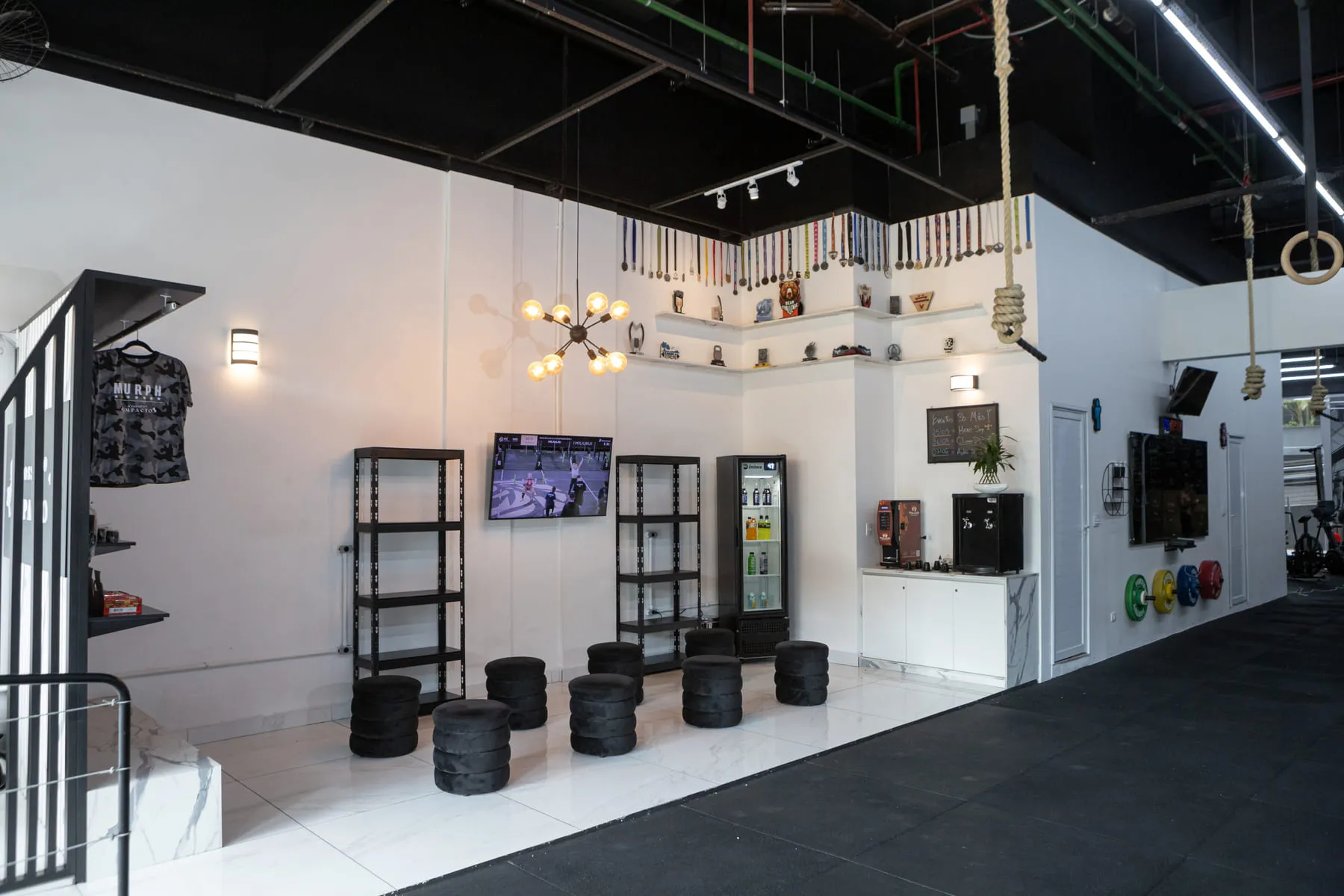 Recepção do box: as medalhas na prateleira alta, a televisão e as banquetas da área de espera.
